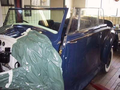 Ein blaues Auto steht mit Plastikfolie abgedeckt in einer Garage.