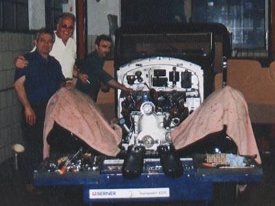 Eine Gruppe von Männern steht um ein Auto mit geöffneter Motorhaube herum