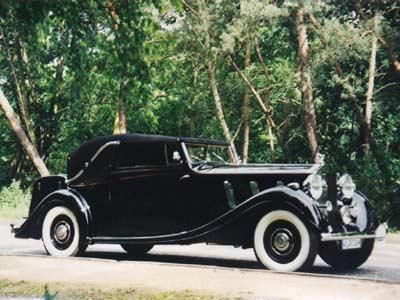 Ein schwarzes Auto mit weißen Reifen ist vor Bäumen geparkt.