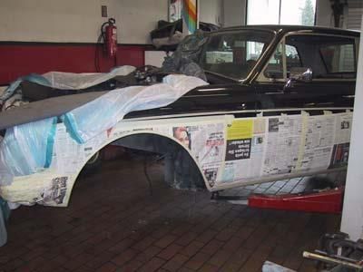 In einer Garage steht ein Auto auf einer Hebebühne und ist mit Zeitungen bedeckt.