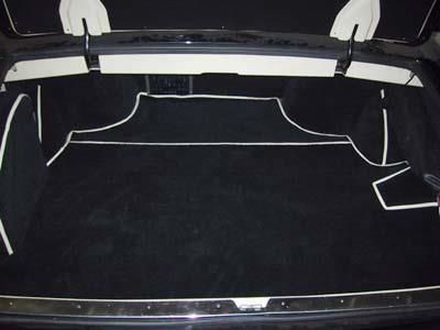 Der Kofferraum eines Autos mit schwarzem Teppich und weißen Zierleisten.