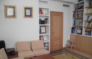 Una sala de estar con un sofá, sillas, estantes y una puerta.