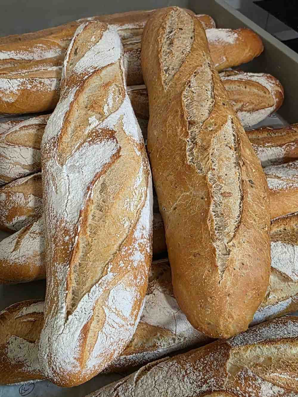 Primer plano de varias baguettes rústicas de color marrón dorado, espolvoreadas con harina.