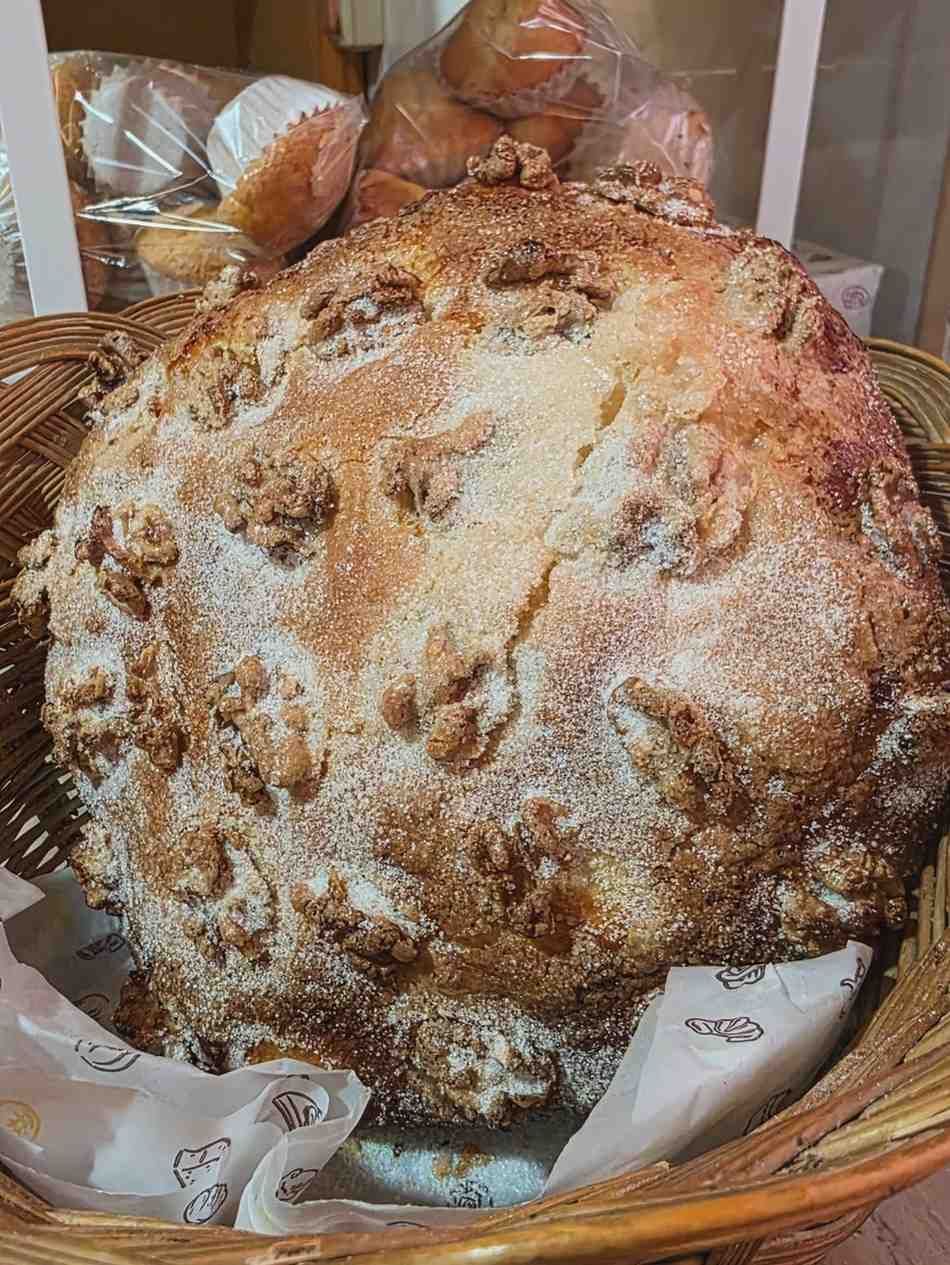 Un gran pan redondo y crujiente, con nueces troceadas, reposando en una cesta de mimbre forrada con papel pergamino.