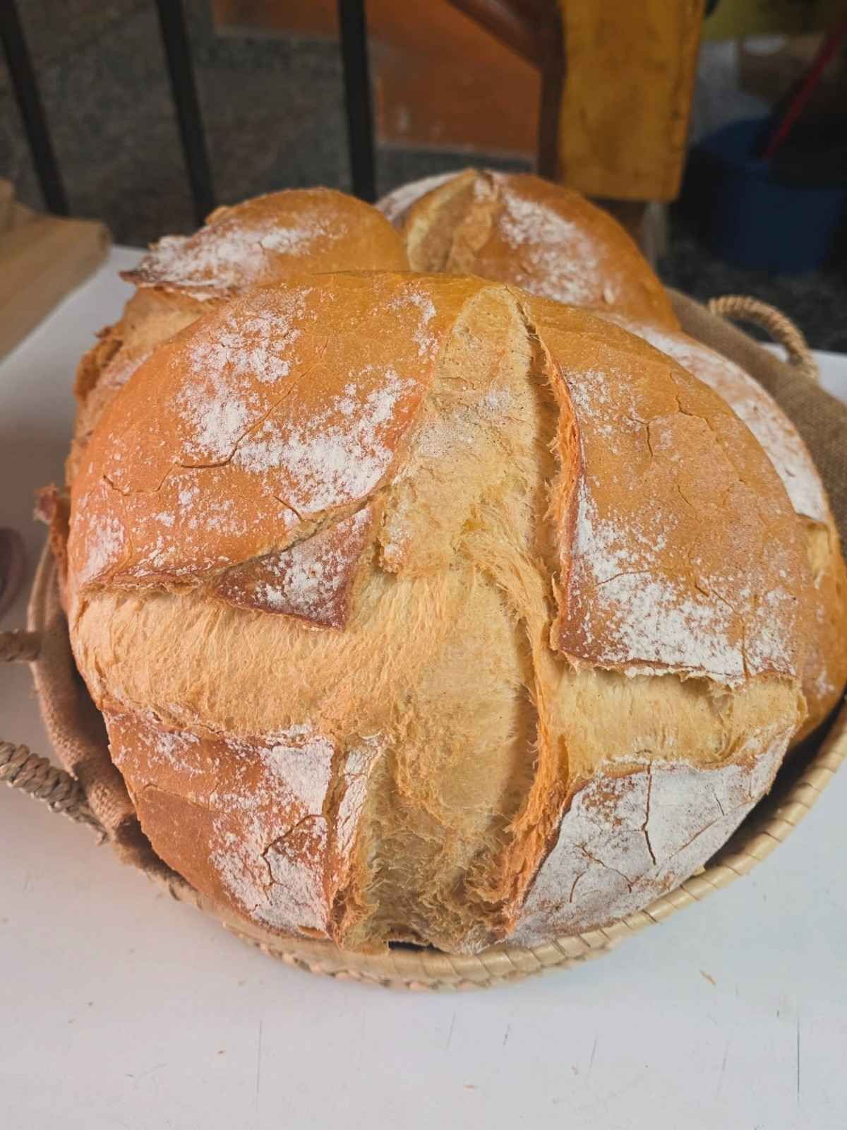 Tres panes redondos de color marrón dorado, colocados en una cesta tejida y forrada con arpillera.