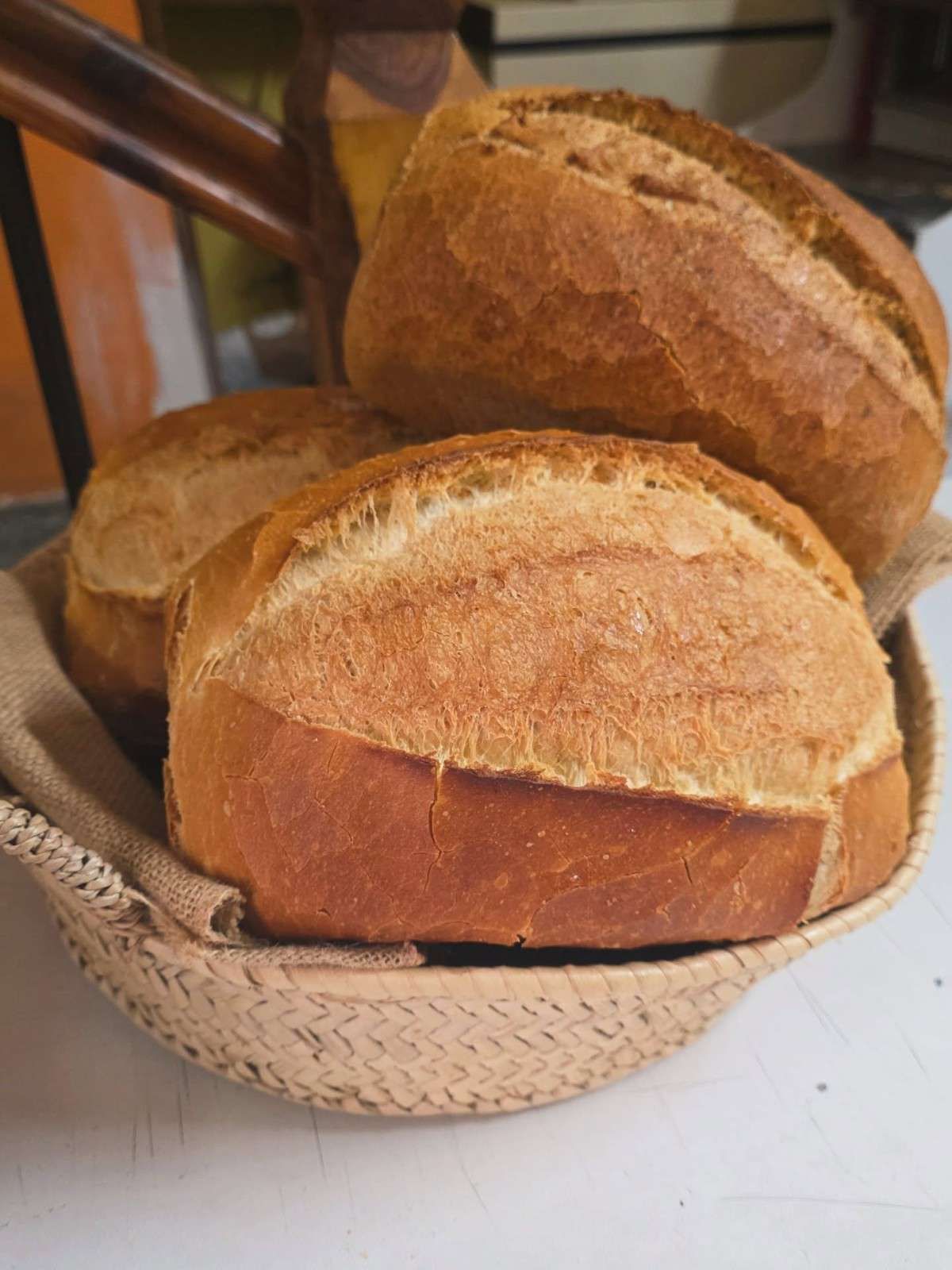 Varias hogazas redondas y rústicas de pan de masa madre con la parte superior marcada, dispuestas en una cesta de mimbre.