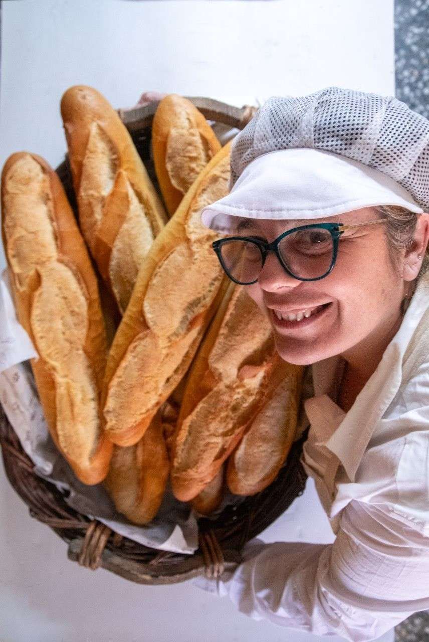 Un gran pan redondo y crujiente, con nueces troceadas, reposando en una cesta de mimbre forrada con papel pergamino.