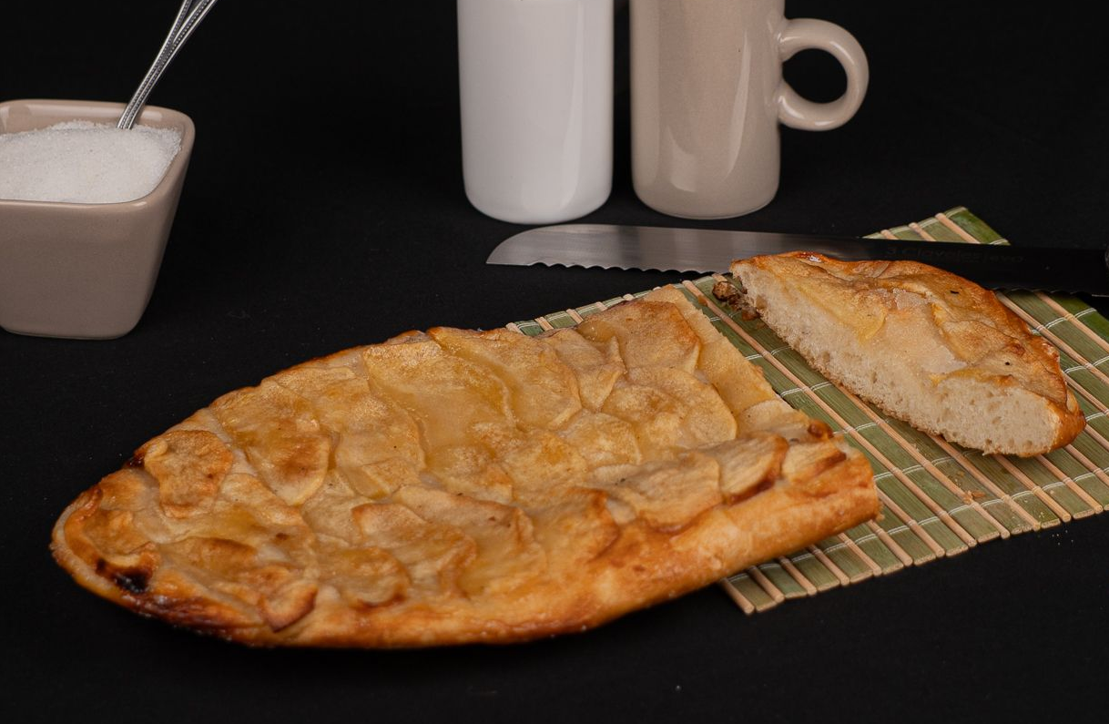 Masa fina de pan coronada con manzana laminada, aceite y azúcar