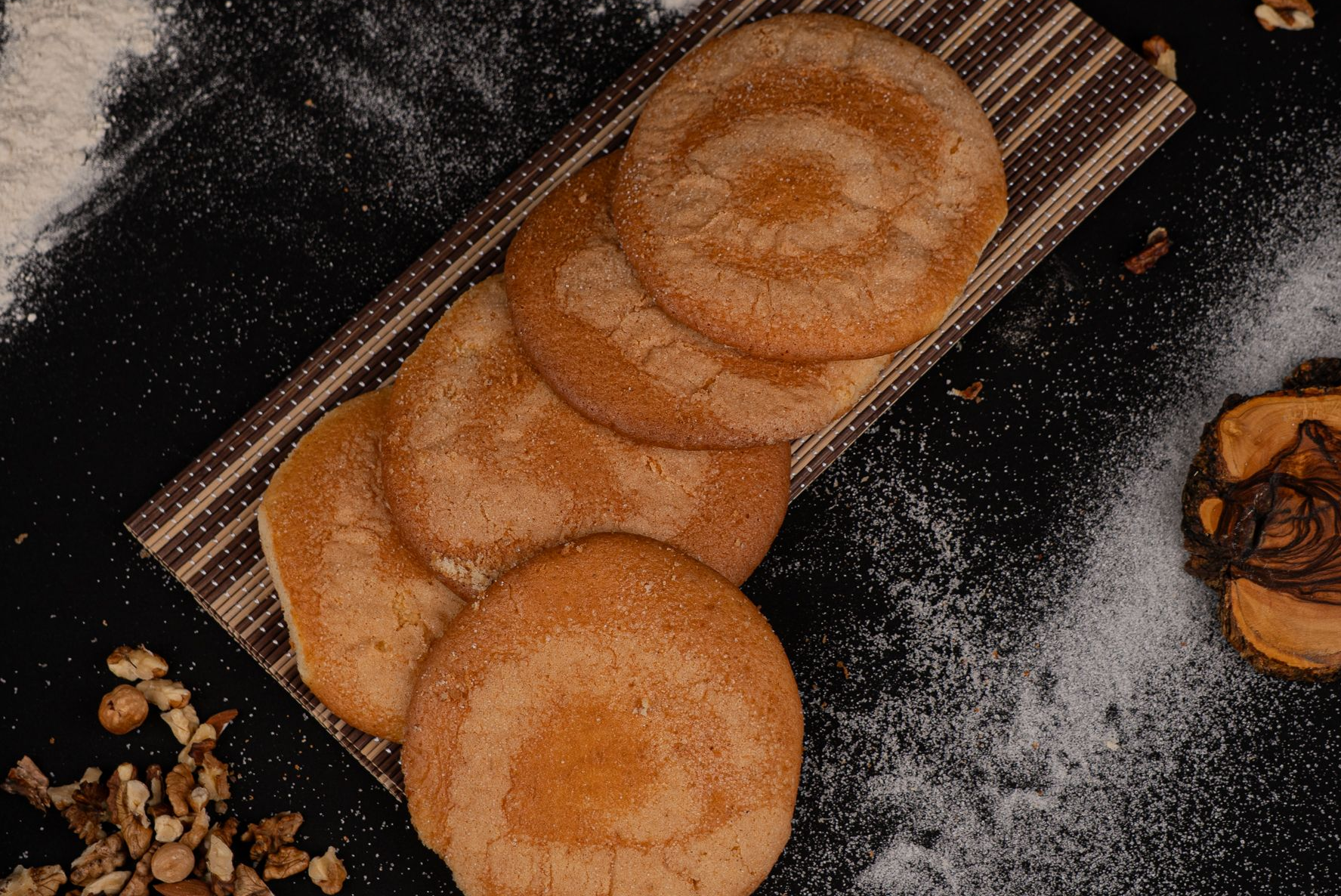 Galletas espolvoreadas con azúcar sobre una bandeja a rayas, con harina esparcida sobre una superficie oscura.