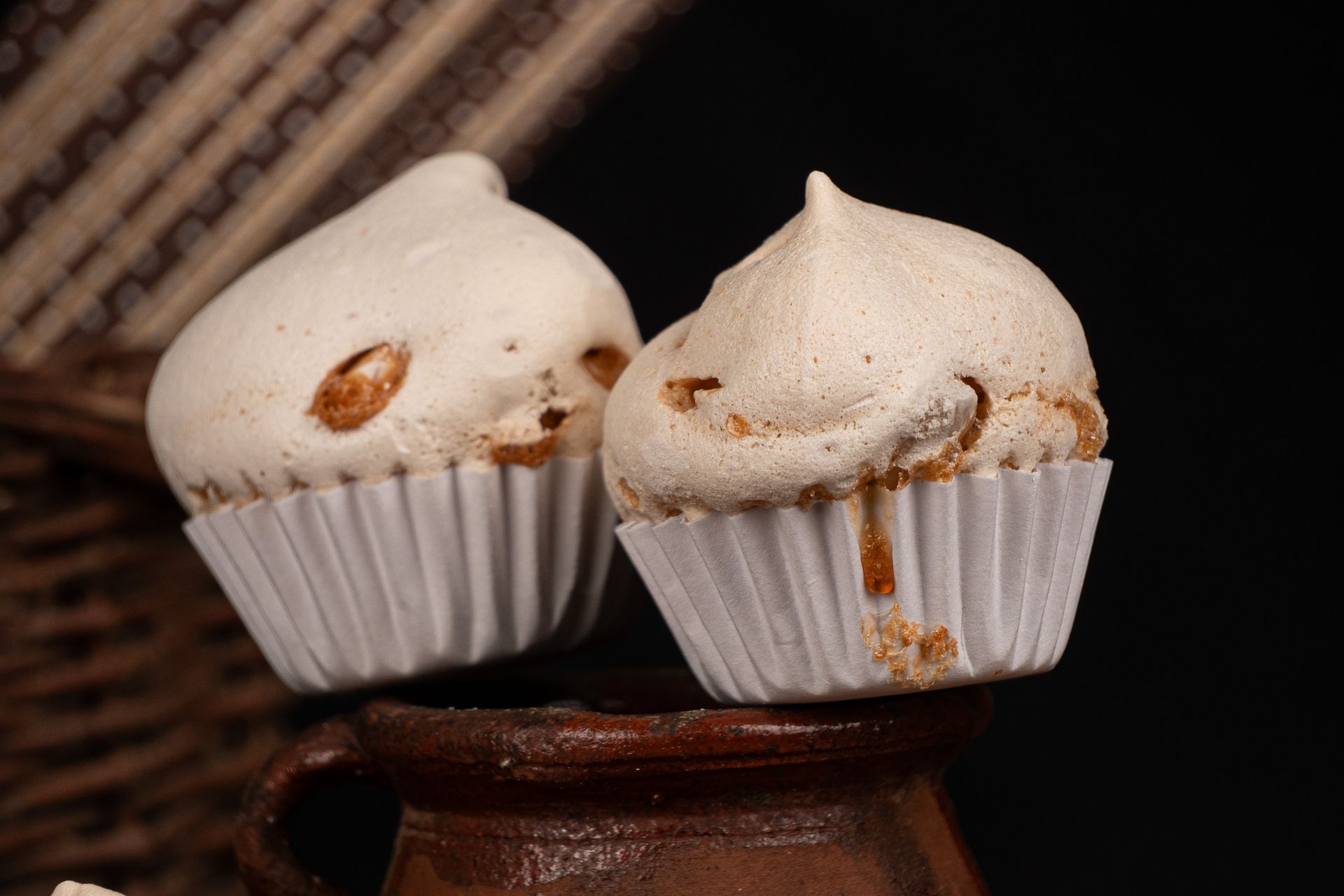 Dos cupcakes blancos glaseados envueltos en papel blanco sobre un soporte de madera oscura.