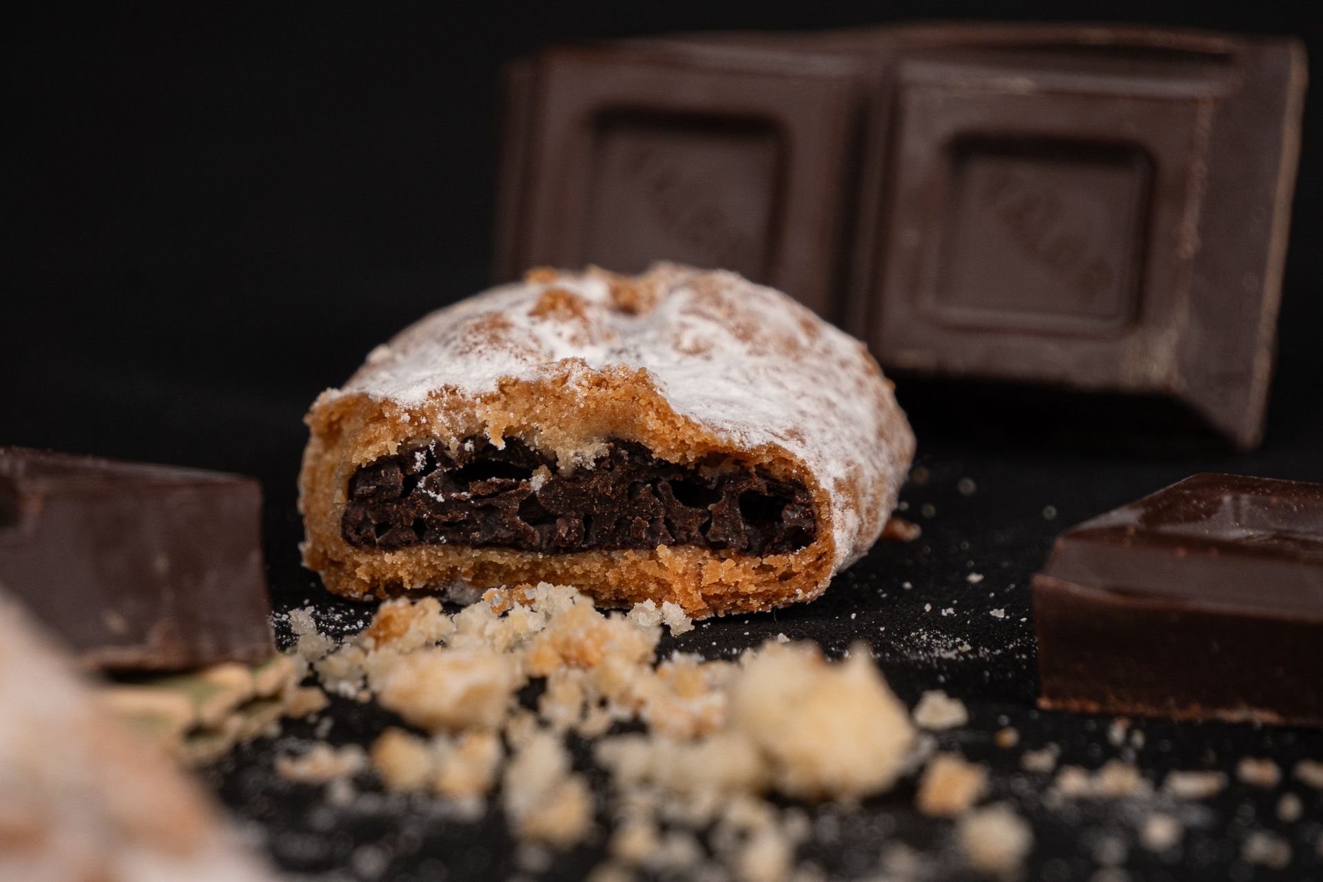 Pastel relleno de chocolate en polvo con trozos de barras de chocolate y migas sobre una superficie oscura.