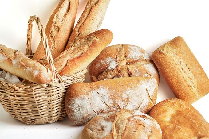 Variedad de panes frescos y baguettes en una cesta sobre un fondo blanco.