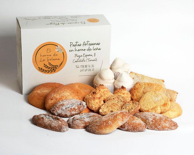 Variedad de pasteles y merengues expuestos frente a una caja de panadería blanca sobre un fondo blanco.