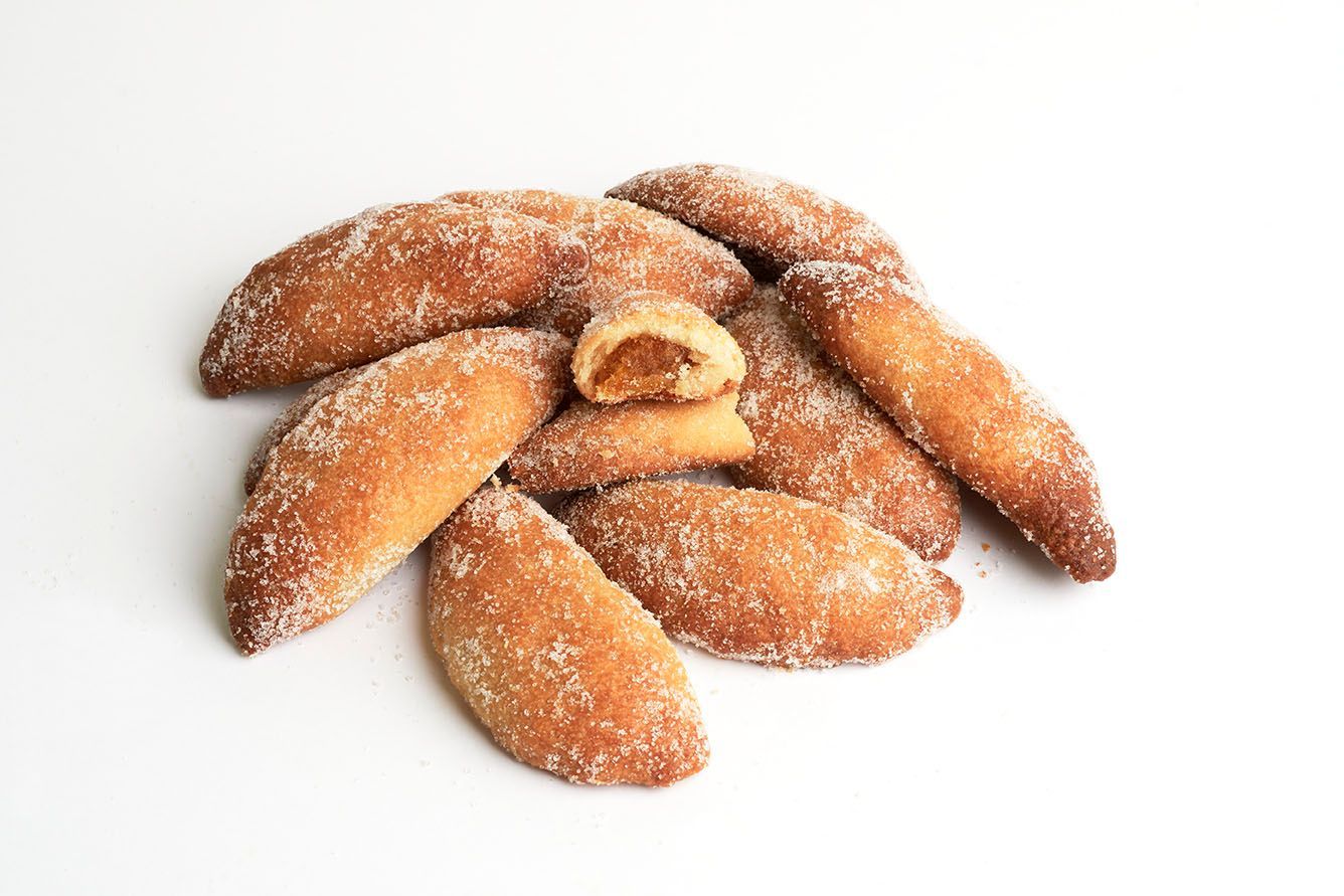 Pasteles cubiertos de azúcar dispuestos sobre un fondo blanco.
Aceite, moscatel, anís y un relleno de calabaza cocinada con miel, una delicia