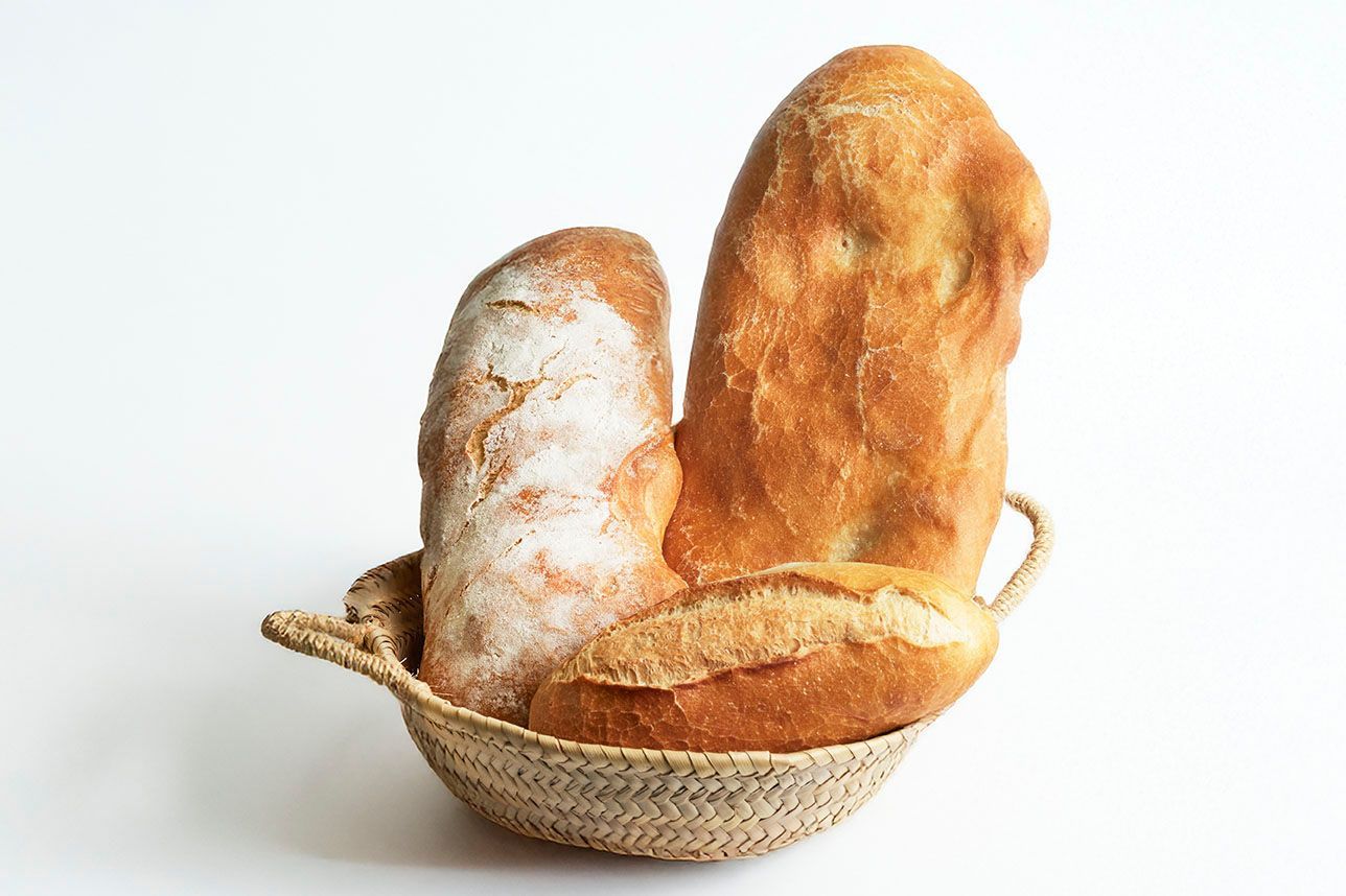 Varias hogazas redondas y rústicas de pan de masa madre con la parte superior marcada, dispuestas en una cesta de mimbre.