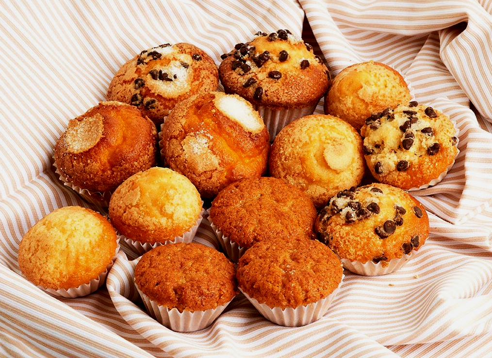 Surtido de magdalenas y cupcakes dorados con pepitas de chocolate sobre un paño a rayas.