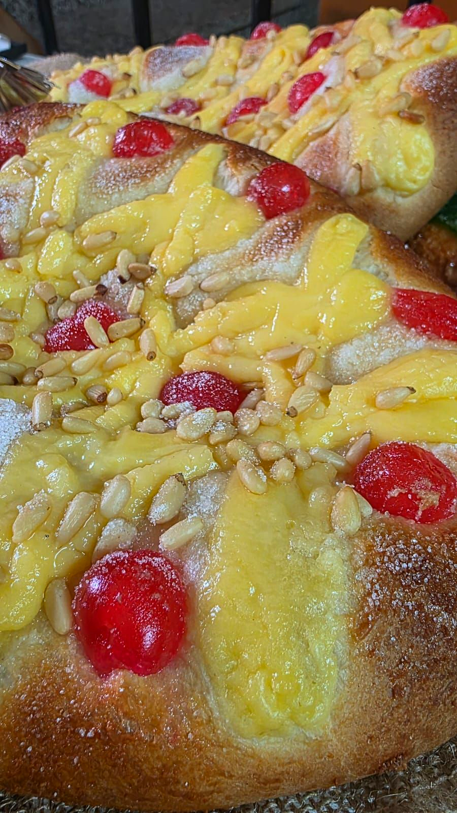 Primer plano de bollos dulces cubiertos con crema pastelera amarilla, cerezas rojas y streusel crujiente.
