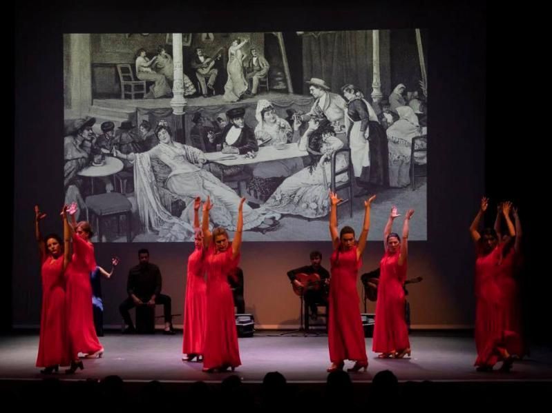 Un grupo de mujeres con vestidos rojos bailan en un escenario frente a una pantalla grande.