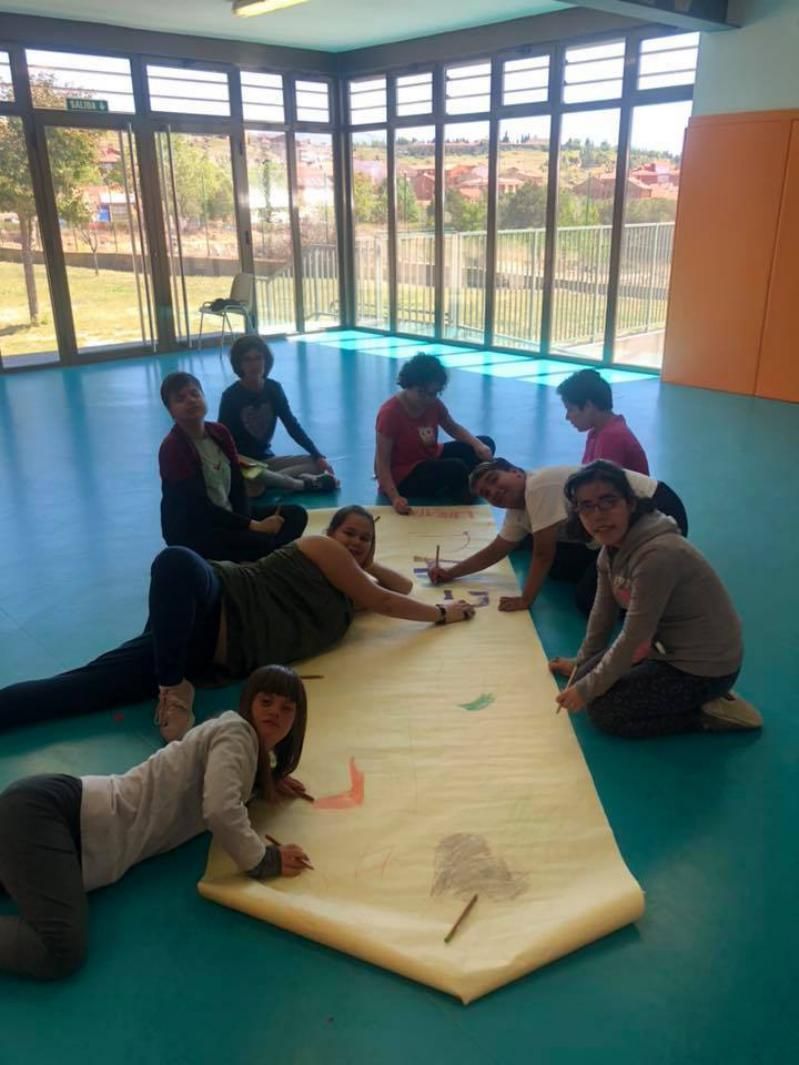 Un grupo de niños están acostados en el suelo dibujando en un trozo grande de papel.