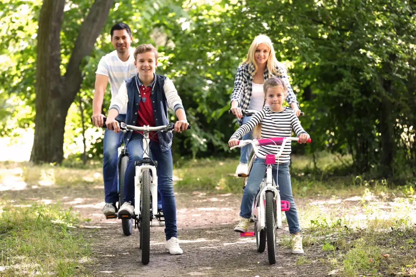 Eine Familie fährt gemeinsam mit Fahrrädern auf einem sonnenbeschienenen Waldweg.