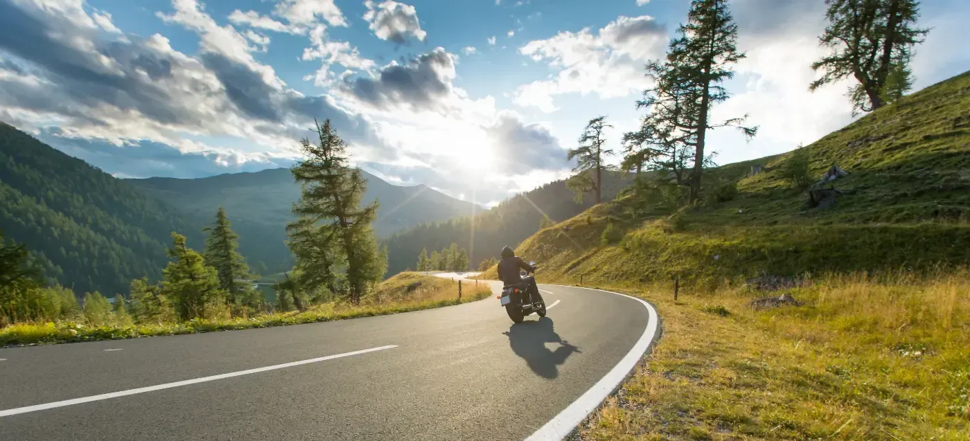 Ein Motorradfahrer fährt an einem sonnigen, goldfarbenen Nachmittag eine kurvenreiche Bergstraße entlang.
