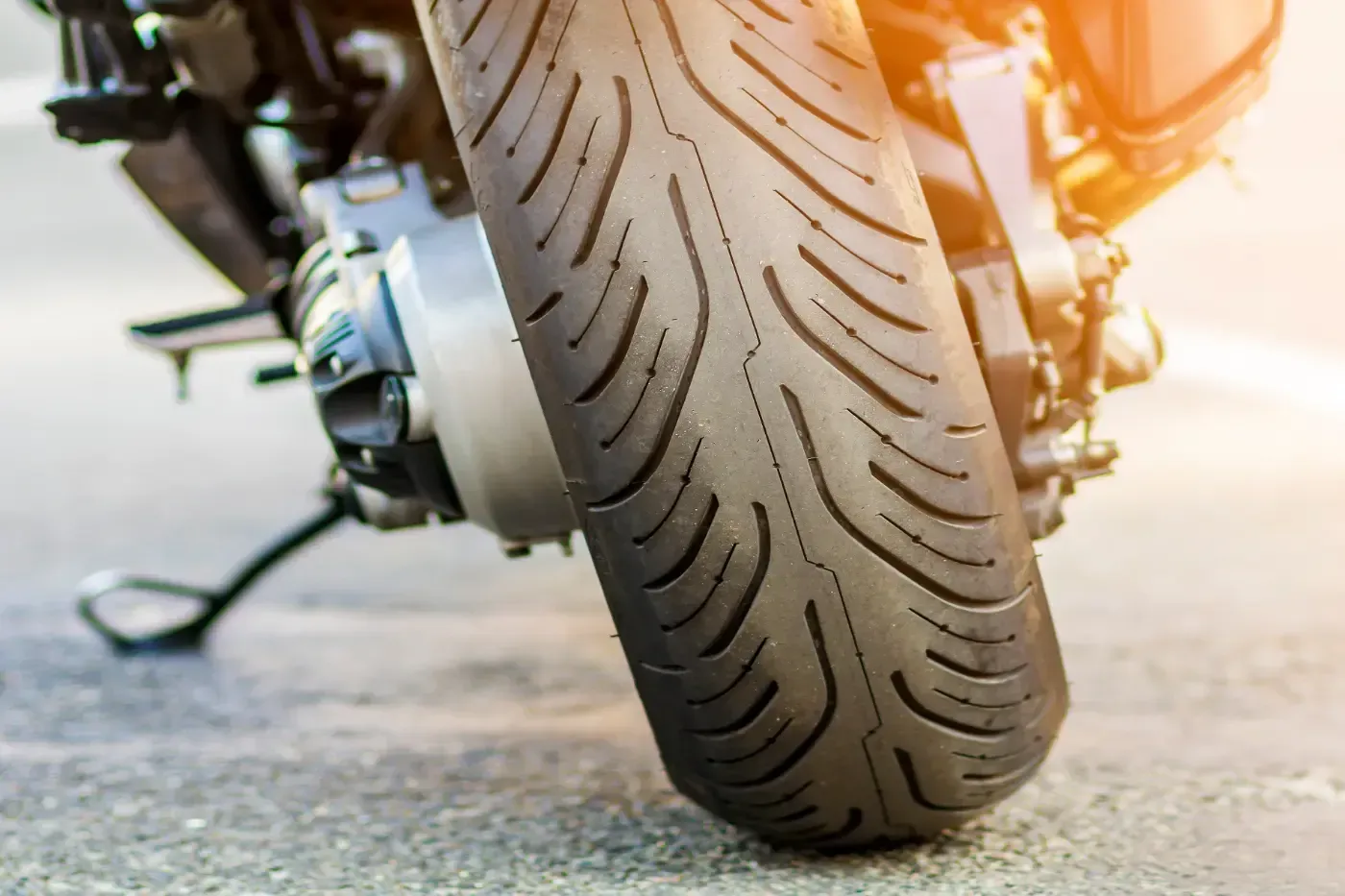 Nahaufnahme aus niedrigem Winkel eines Motorradhinterreifens mit Profil, der auf einer gepflasterten Oberfläche aufliegt.