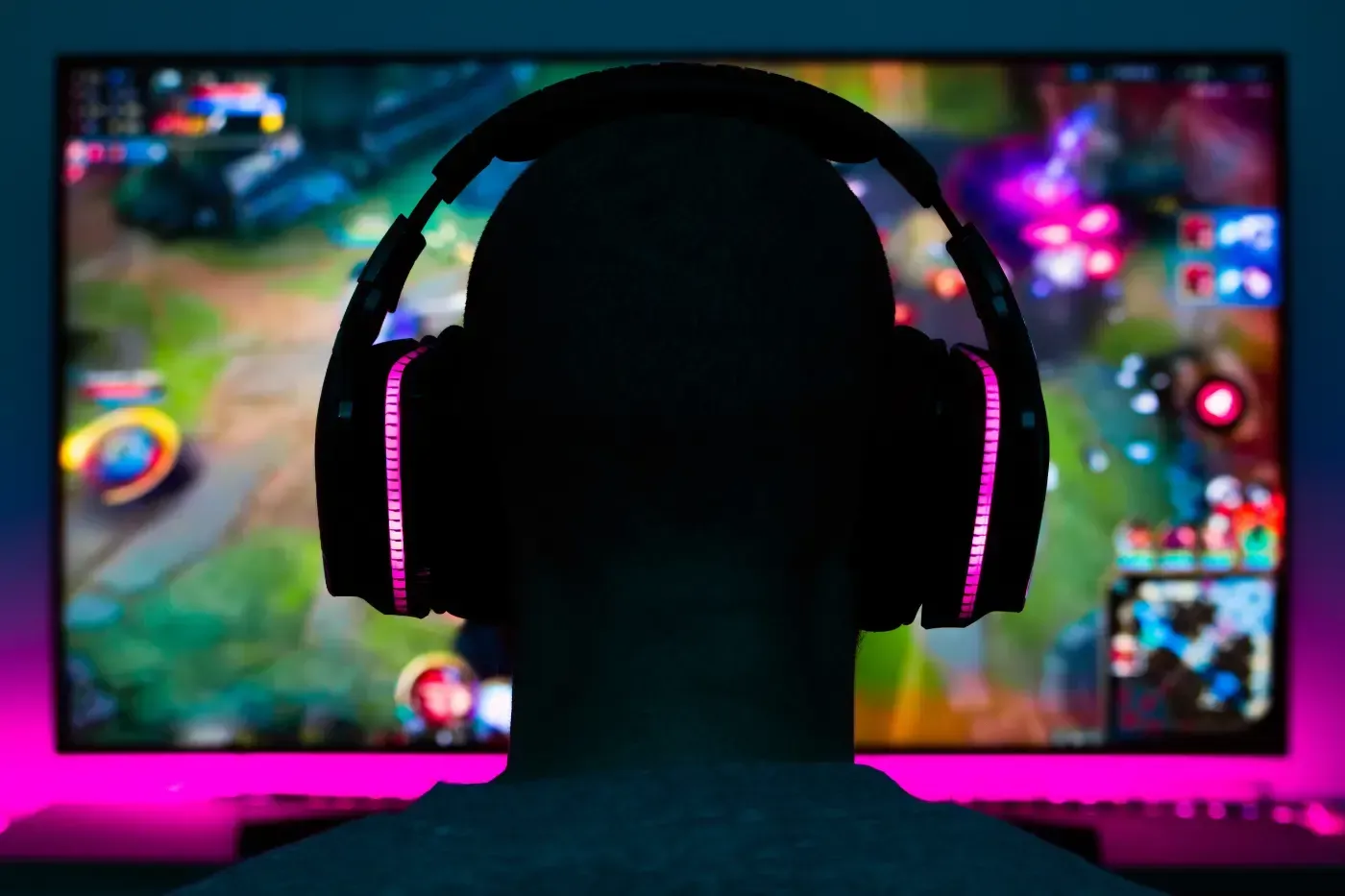 Ein Gamer mit beleuchteten Kopfhörern, von hinten gesehen, blickt auf einen hellen Computerbildschirm, auf dem ein Videospiel angezeigt wird.