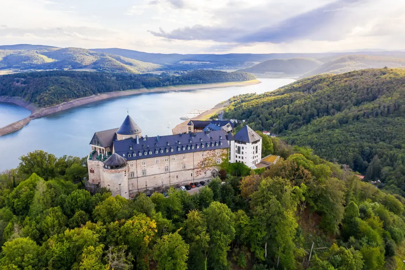 Luftaufnahme der Burg Waldeck, eingebettet in üppige grüne Wälder mit Blick auf ein malerisches Flusstal.