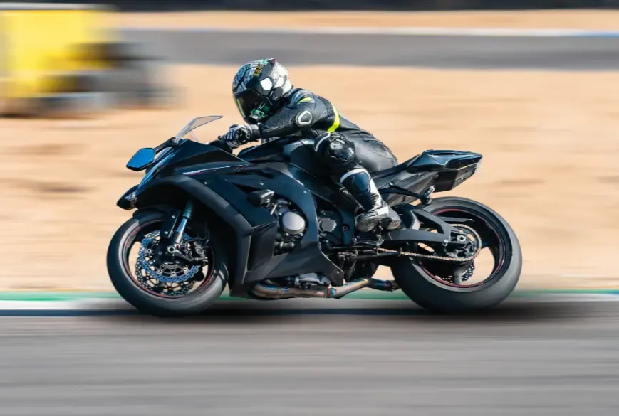 Eine Person in komplett schwarzer Rennmontur fährt ein schwarzes Sportmotorrad auf einer Rennstrecke; die Aufnahme zeigt eine verschwommene Seitenansicht.