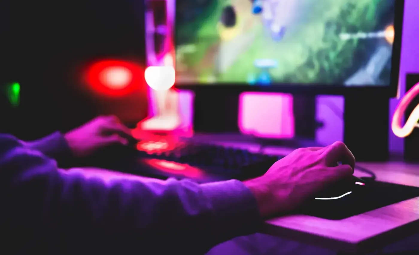 Eine Person spielt ein Computerspiel in einem schwach beleuchteten Raum, der in violettes und rotes Umgebungslicht getaucht ist.