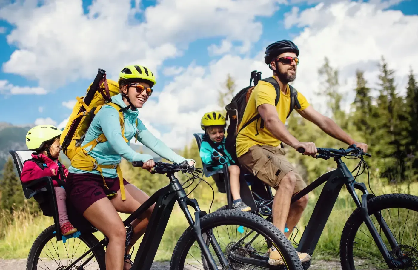 Eine Familie fährt mit elektrischen Mountainbikes auf einem Wanderweg, wobei zwei kleine Kinder in hinten montierten Kindersitzen sitzen.