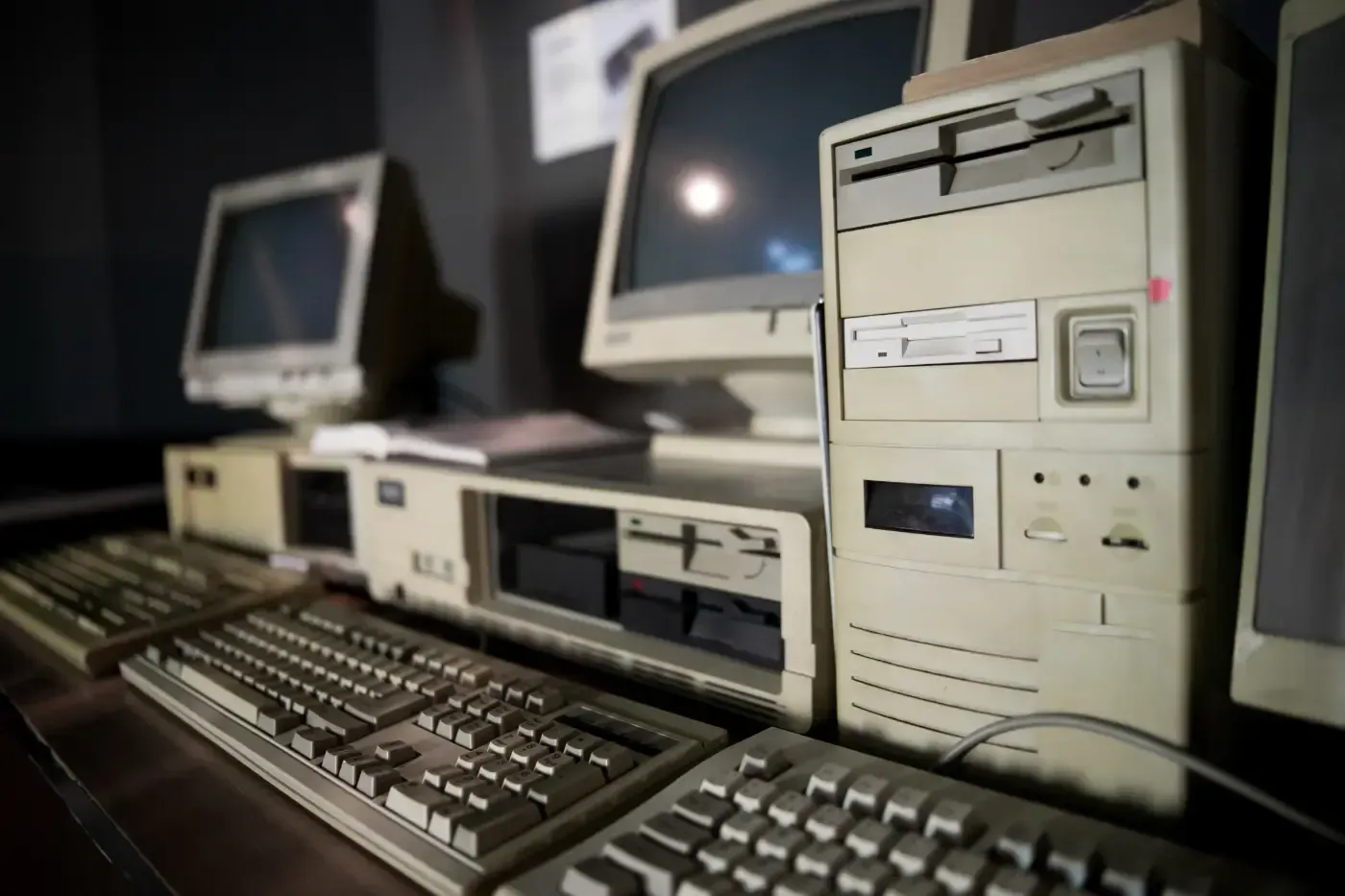 Mehrere beigefarbene Vintage-Desktop-Computer mit klobigen Monitoren und Tastaturen sind auf einer dunklen Fläche angeordnet.