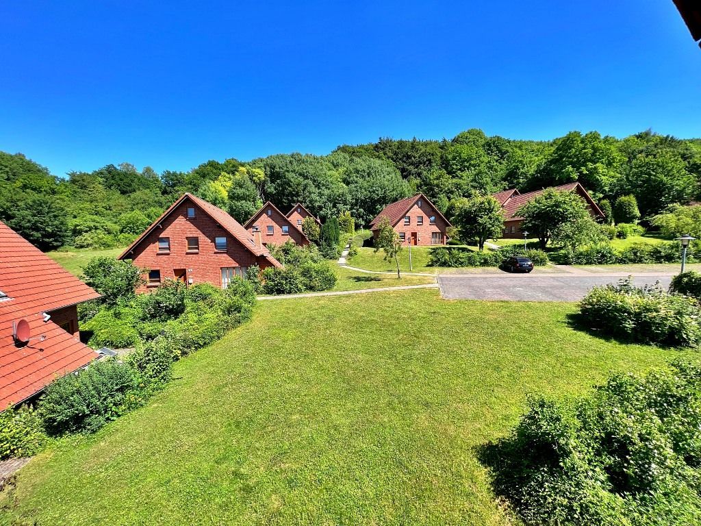 Ferienhäuser mit roten Dächern schmiegen sich in eine üppige, grüne, sonnendurchflutete Landschaft vor einem klaren blauen Himmel.