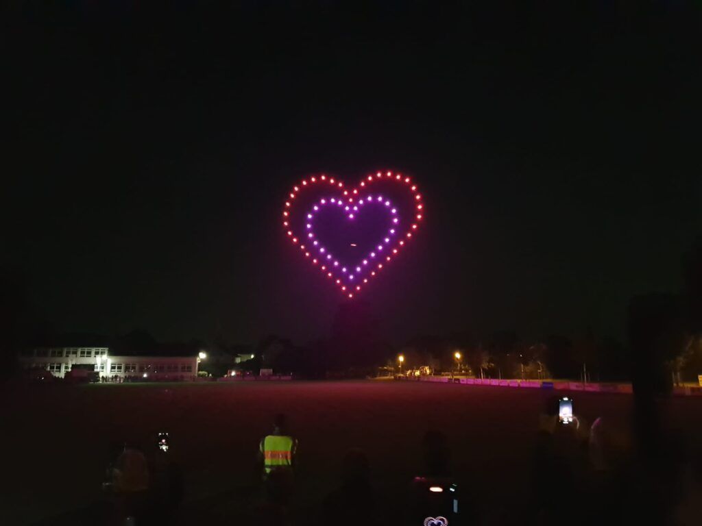 Eine leuchtende, zweischichtige, rot-violette, herzförmige Drohnenformation hob sich gegen den Nachthimmel über einem dunklen Feld ab.