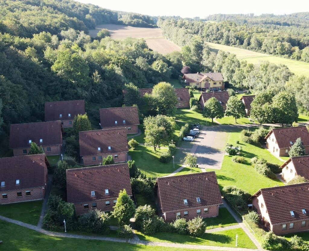 Luftaufnahme einer Wohnanlage mit rotgedeckten Backsteingebäuden, eingebettet in grüne Bäume und mit einem zentralen Parkplatz.