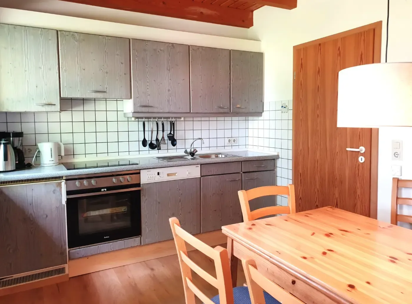 Eine Küche mit grauen Schränken, einem Edelstahlofen, einem gefliesten Spritzschutz und einem Esstisch aus Holz im Vordergrund.