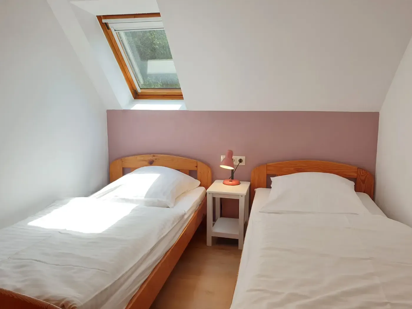 Ein Schlafzimmer mit zwei Einzelbetten mit weißer Bettwäsche, einem kleinen weißen Nachttisch mit Lampe und einem Dachfenster.
