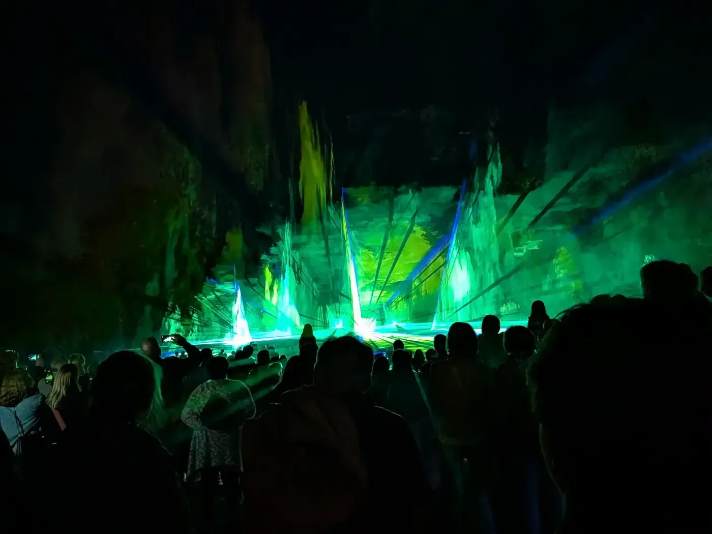 Eine große Menschenmenge beobachtet abends eine Fontänenshow im Freien mit hellgrünen Scheinwerfern und beleuchteten Wasserstrahlen.