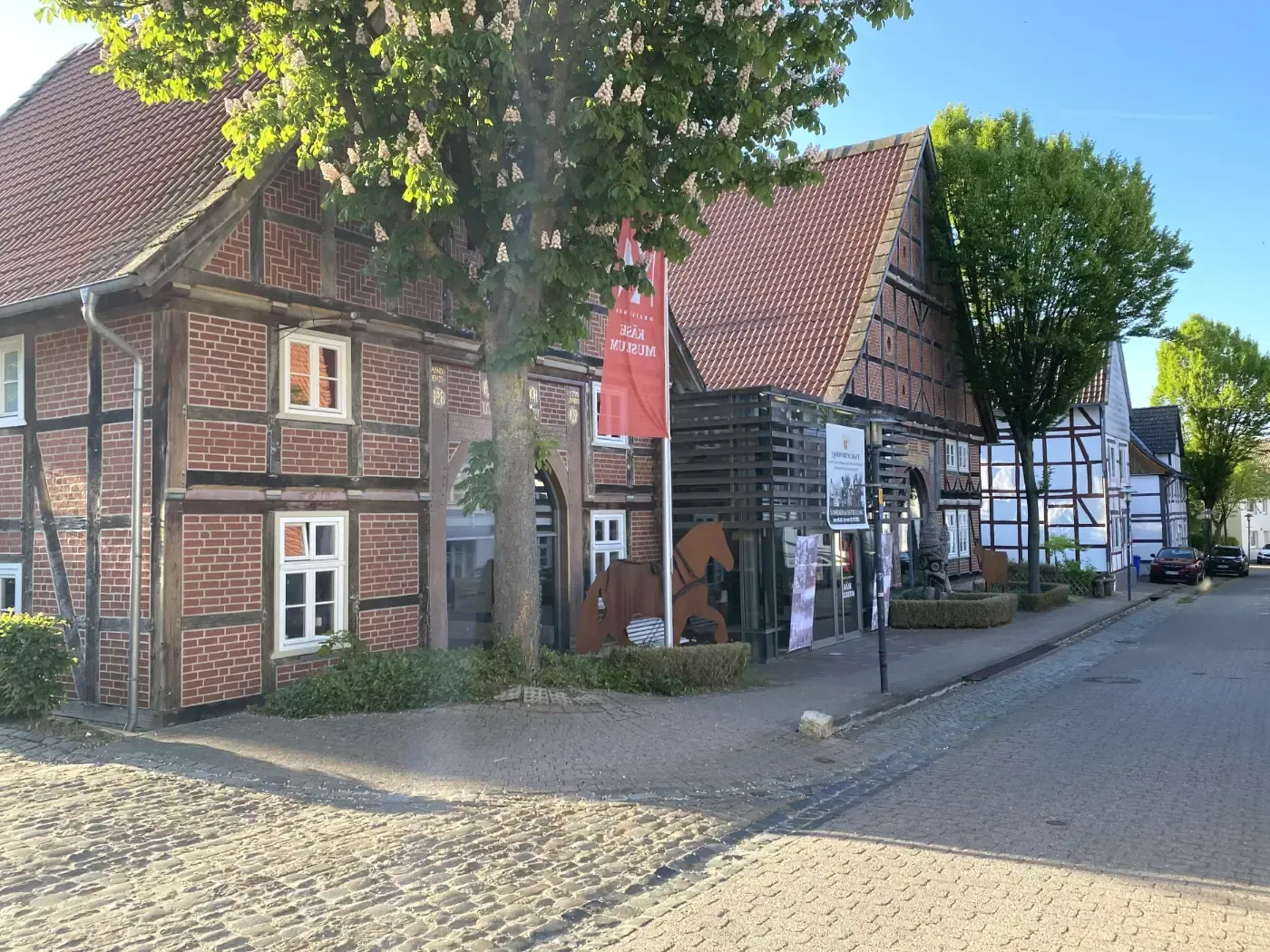Ein sonniger Straßenblick auf traditionelle Fachwerkhäuser aus Backstein mit roten Ziegeldächern und weiß gerahmten Fenstern.