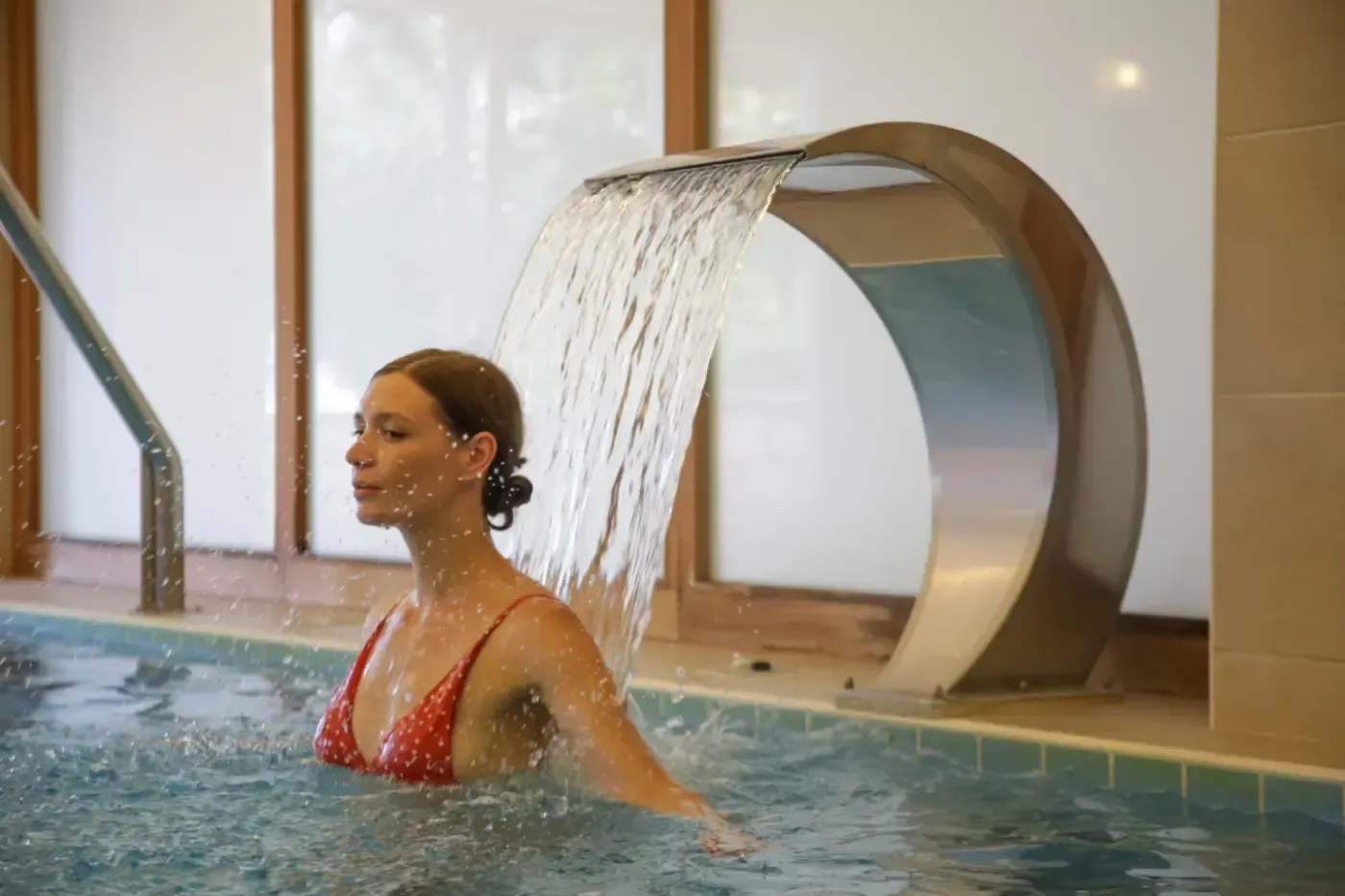 Eine Person entspannt mit geschlossenen Augen in einem Pool unter einem Wasserfall aus Edelstahl.