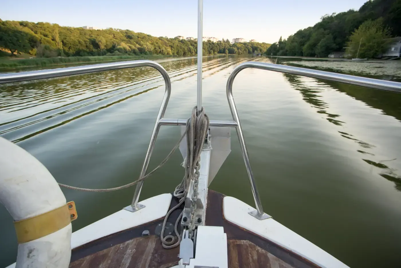 Blick vom Bug eines Bootes, das durch ruhiges Wasser fährt, mit bewaldeten Ufern auf beiden Seiten.