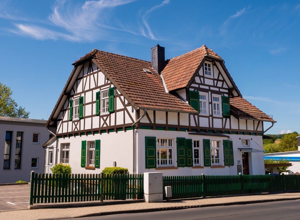 Weißes Fachwerkhaus mit grünen Fensterläden und rotem Ziegeldach an einer Straßenecke unter blauem Himmel