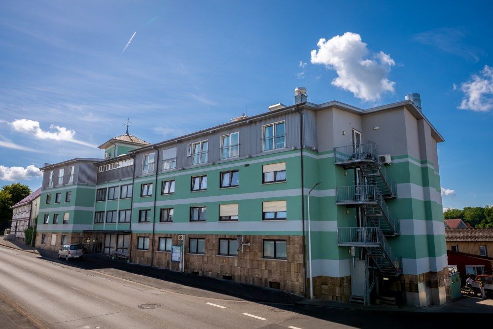 Langes grünes Wohnhaus mit Außentreppe entlang einer Straße unter blauem Himmel