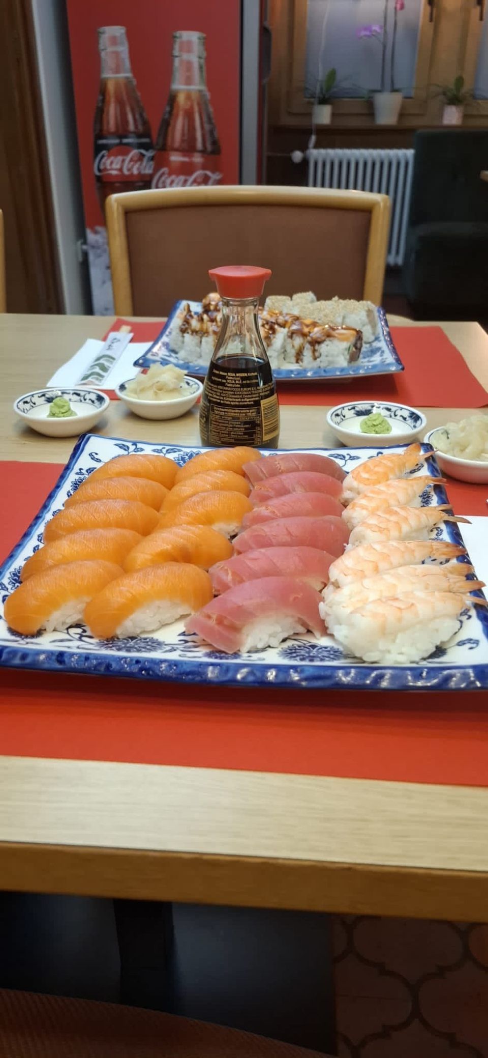 Sushi-Platte mit Lachs-, Thunfisch- und Garnelen-Nigiri, Sojasauce und Rollen auf einem Tisch.