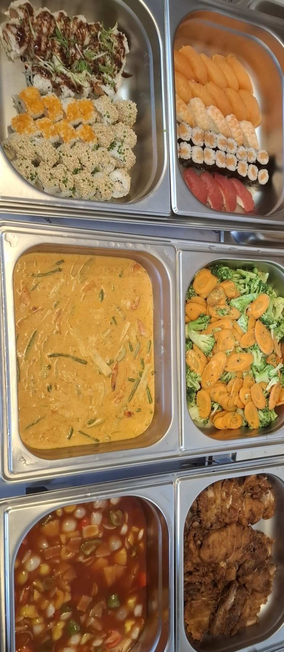 Sushi und andere Speisen in Servierbehältern aus Metall.