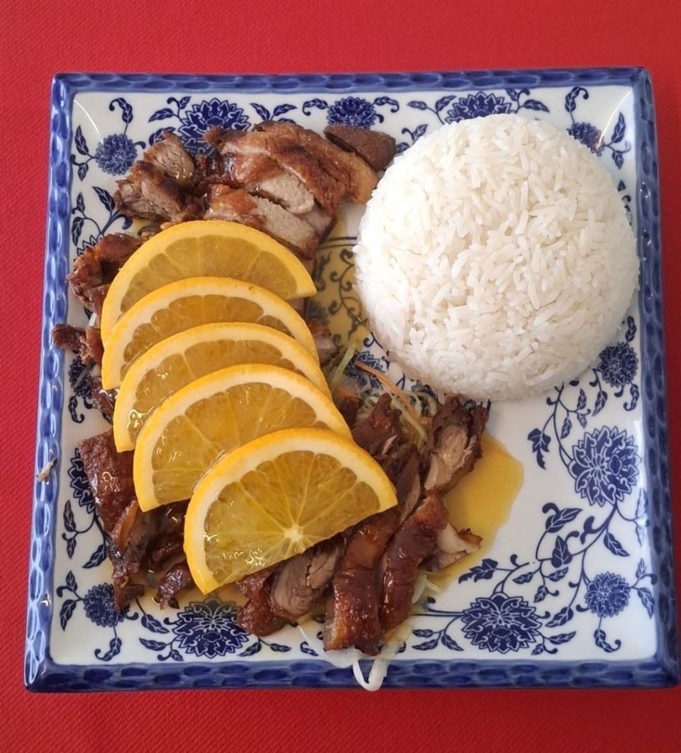 Ente mit Orangenscheiben und Reis auf einem gemusterten blau-weissen Teller.