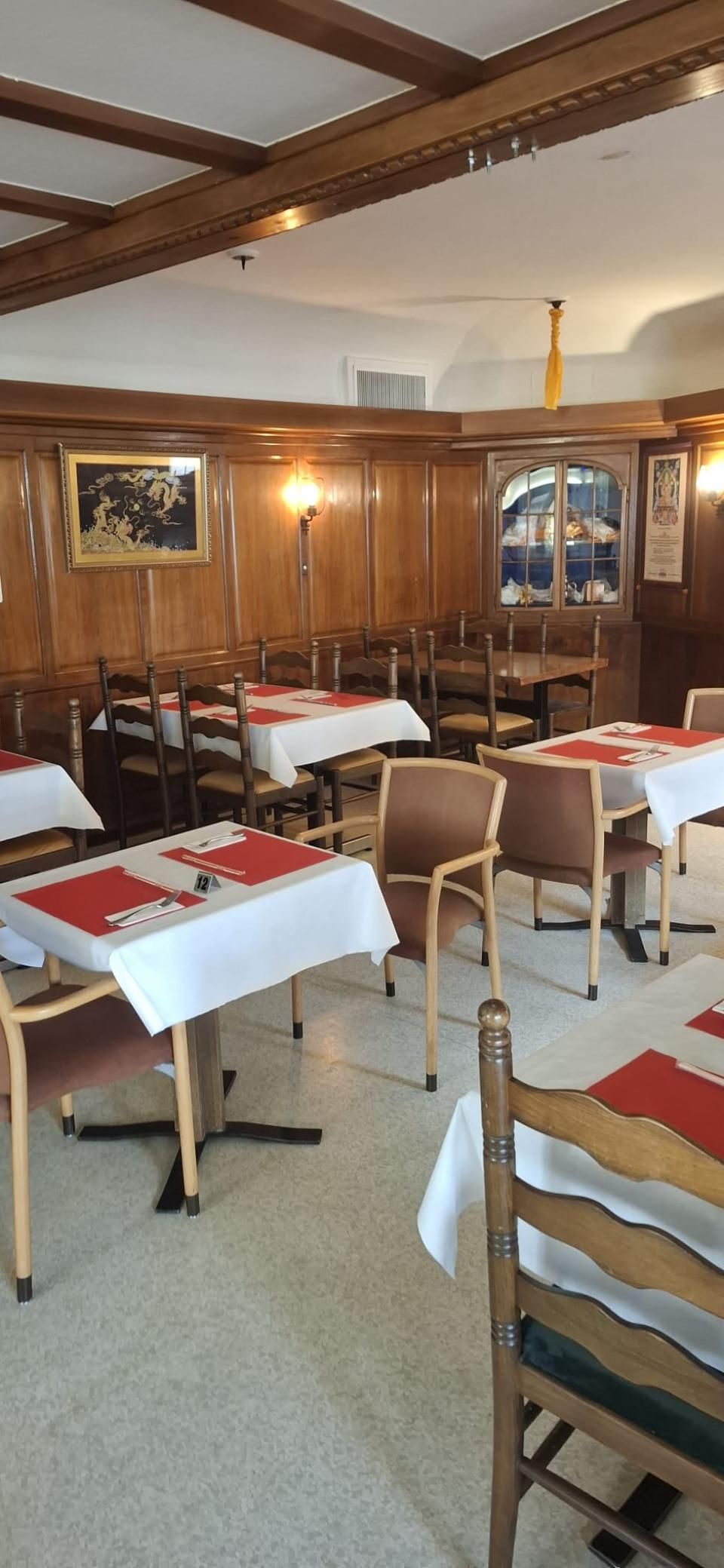 Restaurant-Speisesaal mit gedeckten Tischen; Holzvertäfelung und Deckenbalken; rote Platzsets.