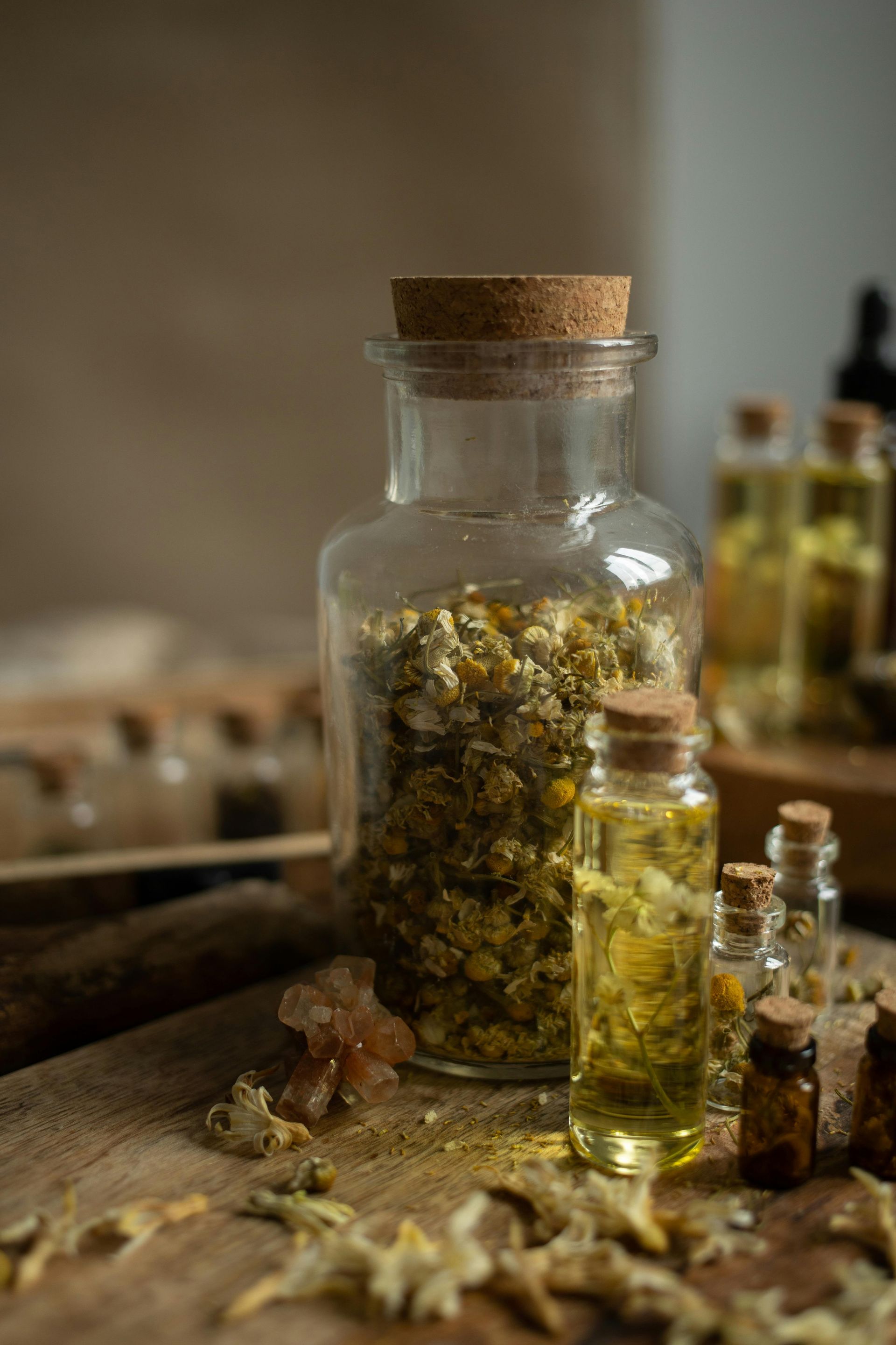 Un frasco de vidrio lleno de flores secas y una botella de aceite sobre una mesa de madera.