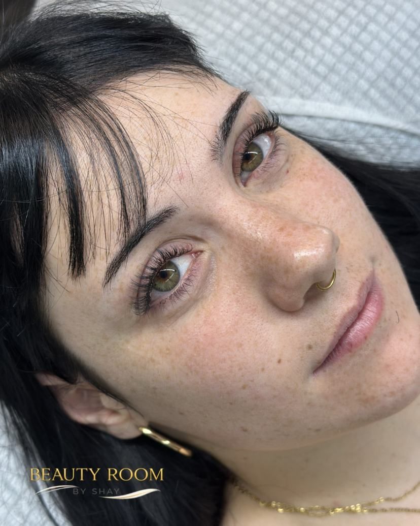 Primer plano de una mujer con cabello oscuro, pecas claras y ojos verdes, recostada sobre una almohada, mirando a la cámara.