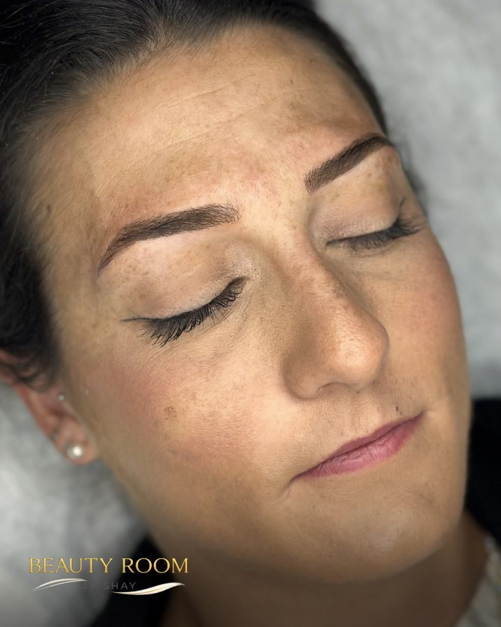 Primer plano de una mujer con los ojos cerrados y maquillada, recostada en una camilla de tratamiento en un salón de belleza.